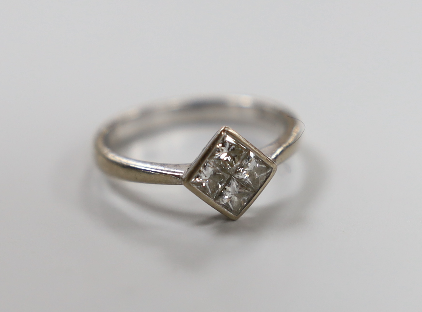 A modern 18ct white gold and four stone princess cut diamond cluster set ring, size L/M, gross 2.6 grams.